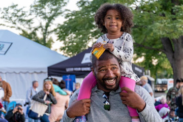 little girl sitting on her dad's shoulders at a festival